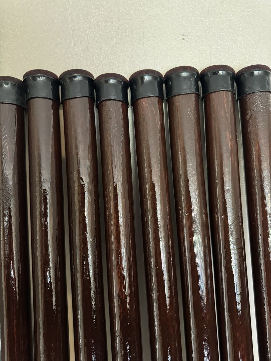Eight finished wooden poles laid side by side, each with a black rubber end cap