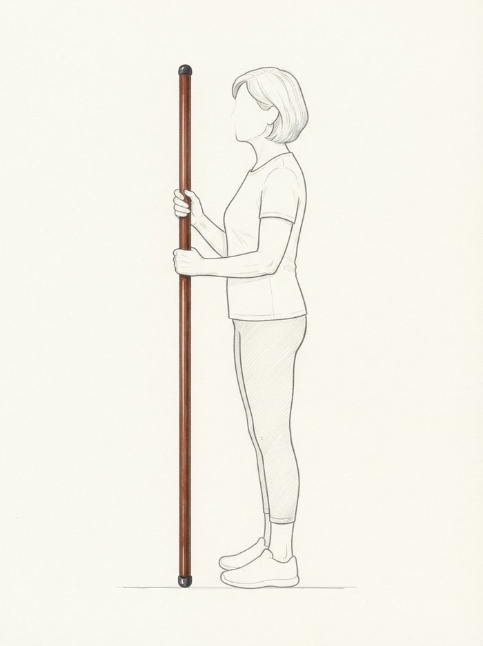 Standing upright holding the pole vertically alongside